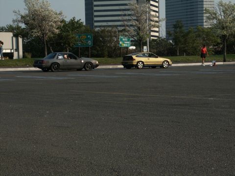 2001 Mercury Grand Marquis - Two cars are parked on a paved lot with buildings and trees in the background.