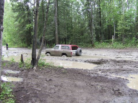 1989 Ford Bronco - A Ford Bronco is stuck in a muddy forest road, with a person standing in the background.