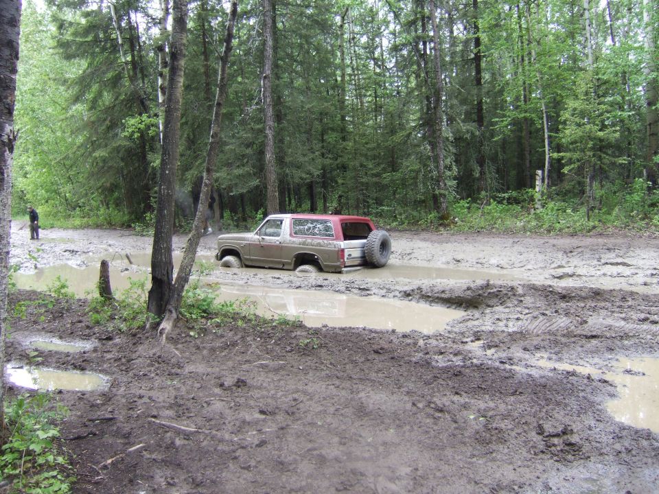 Tan and red Ford Bronco stuck in mud, spare tire on rear