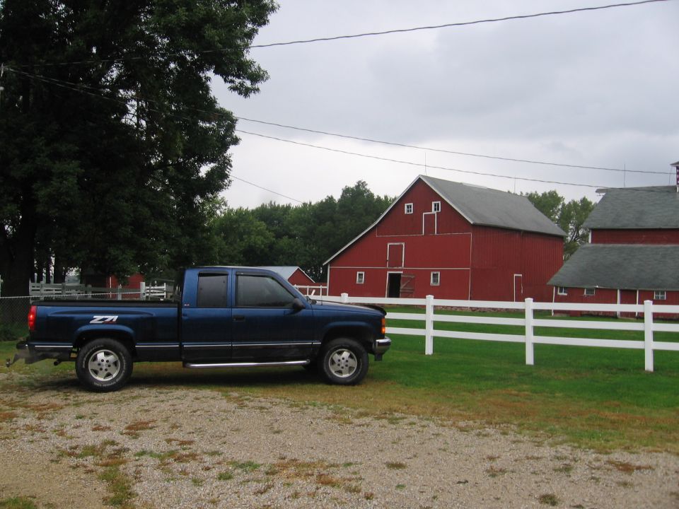 Dark blue Chevrolet Z71 extended-cab pickup parked on gravel in front of a red barn