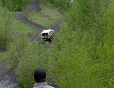 1989 Ford Bronco - A white SUV navigates a challenging dirt track surrounded by dense green foliage.