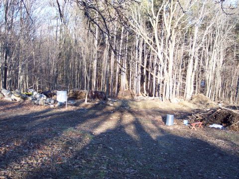 2001 Ford Crown Victoria - A rural scene with trees, logs, rocks, and a metal barrel in the foreground.