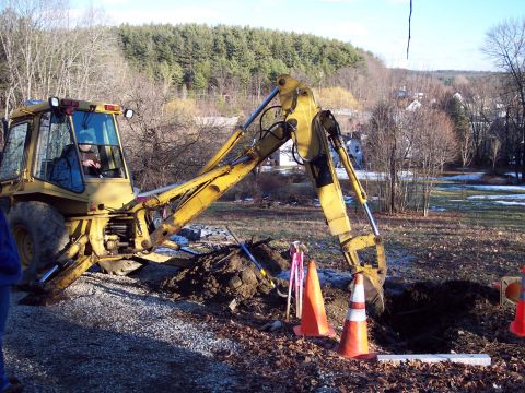 2001 Ford Crown Victoria - A backhoe loader is actively digging a trench in a rural setting with trees and houses visible.