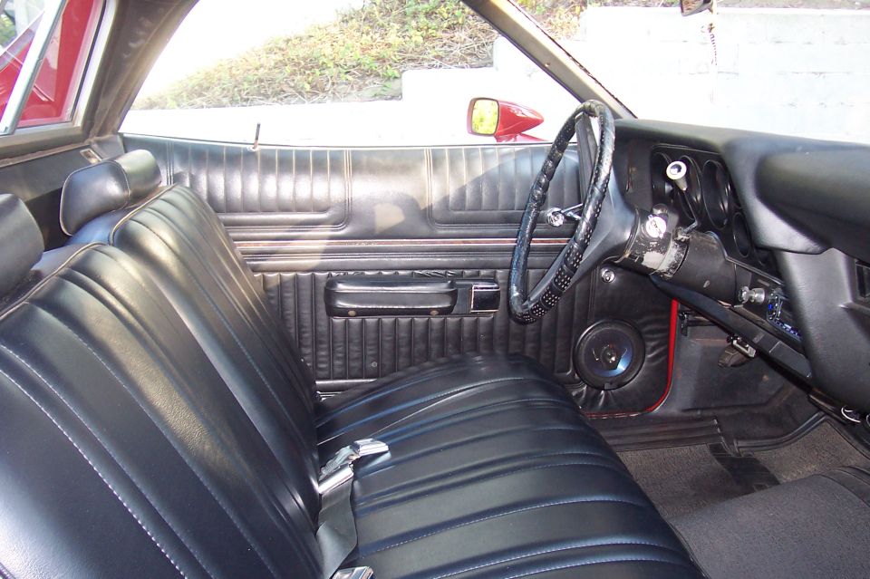 Black vinyl bench-seat interior of a classic car with a lace-wrapped wheel