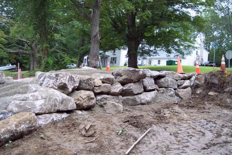 2001 Ford Crown Victoria - A scene of a rock wall being constructed with heavy stones and dirt, set against a backdrop of trees and a house.