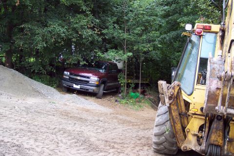 2001 Ford Crown Victoria - A maroon Chevrolet Silverado pickup truck is parked near trees, with a yellow excavator visible in the foreground.