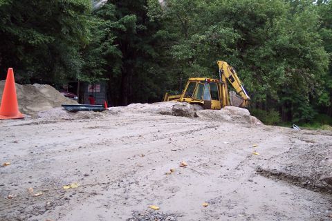 2001 Ford Crown Victoria - A yellow backhoe loader sits partially submerged in a mound of dirt at a construction site, with trees in the background.