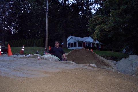 2001 Ford Crown Victoria - A man stands amidst a construction scene with dirt piles and traffic cones, a house visible behind trees.