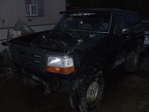 1989 Ford Bronco - This dark-colored Ford Bronco is parked outside with its hood open, revealing the engine bay.