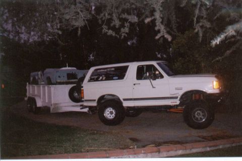 1966 Ford Bronco - Night side view of a white lifted Ford Bronco with removable hardtop, side pinstripe, tinted rear side glass and a rear-mounted spare, park…