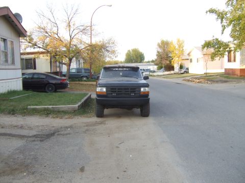 1989 Ford Bronco - This black Ford Bronco is parked on a residential street with houses and trees visible.