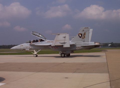 2003 Ford Crown Victoria - A Navy F/A-18 Hornet fighter jet sits on the tarmac with its canopy open, displaying its markings.
