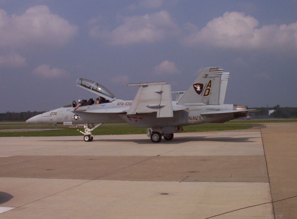 Navy F/A-18 Hornet jet on tarmac, canopy open. Tail has 'AD' and a shield emblem
