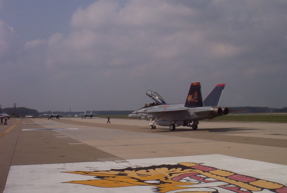 Fighter jet on an airport runway with other aircraft in the background