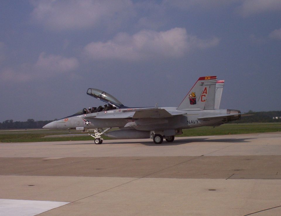Navy fighter jet on tarmac, canopy open. Tail has AC markings