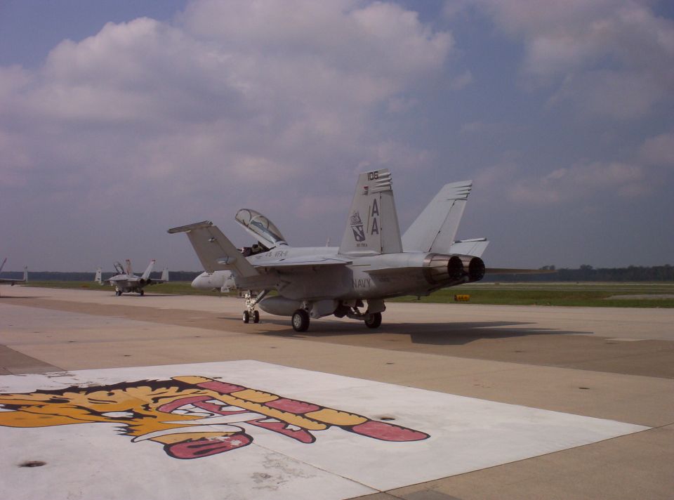 Gray fighter jet on tarmac with open canopy and visible markings