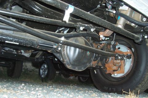 1994 Ford F-150 - Undercarriage view of a truck's front axle and suspension system, with another vehicle visible in the background.