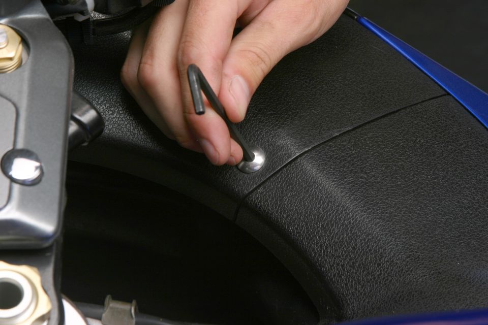 Hand using an Allen key on a fastener in black plastic bodywork of a Suzuki Hayabusa