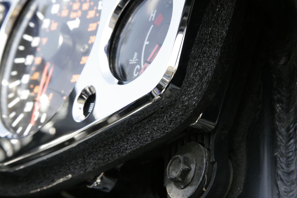 Close-up of chrome-trimmed temperature gauge and speedometer edge on a motorcycle instrument cluster