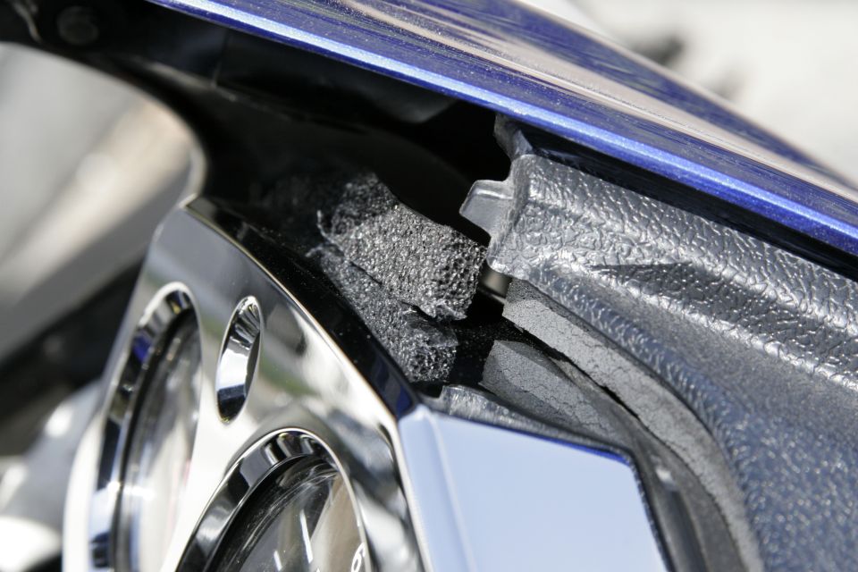 Close-up of cracked black motorcycle fairing with exposed gray foam and blue paint