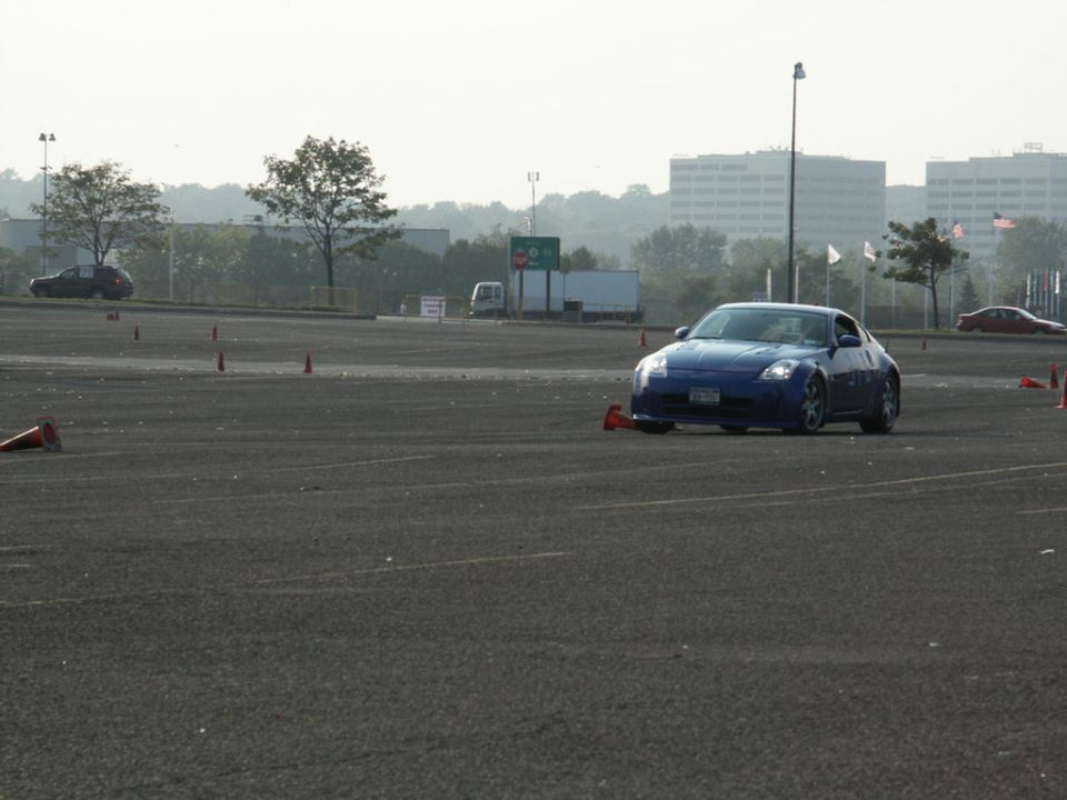 Blue sports car on asphalt with orange cones, buildings in background