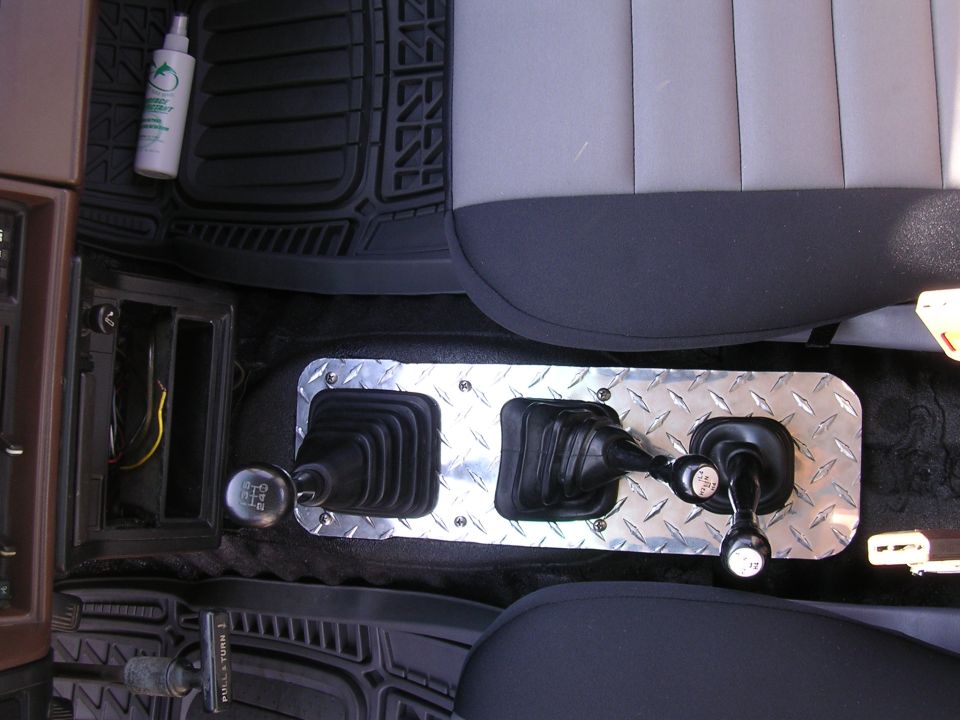 Interior shot of a vehicle's center console with two gear shifters and a diamond plate trim. A bottle of cleaner sits on the floor mat