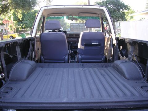 1985 Toyota 4Runner - The interior of a white pickup truck, showing the bed liner and front seats, with a glimpse of the dashboard.