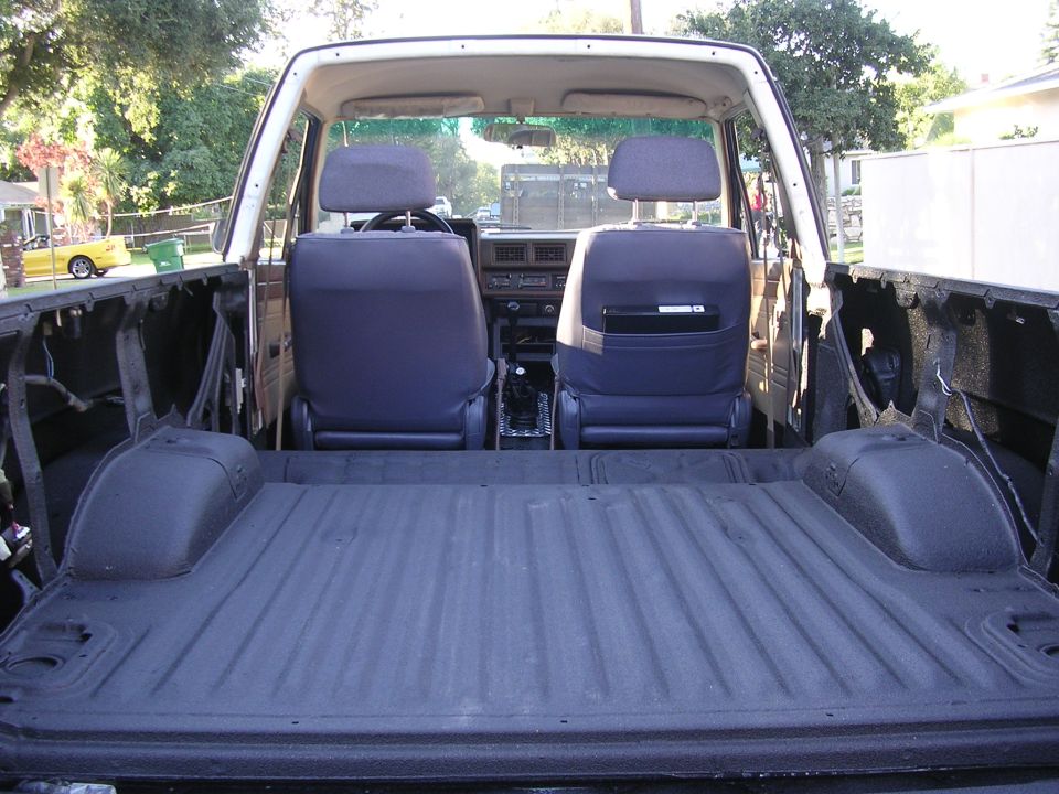 Rear cargo area of a small SUV coated in black bedliner, blue bucket seats ahead, top removed