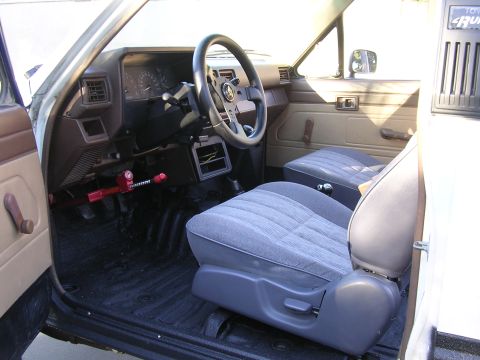 1985 Toyota 4Runner - The interior of a 1985 Toyota 4Runner shows grey cloth seats and an aftermarket steering wheel with a red anti-theft device.