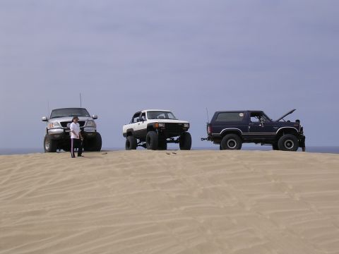 1985 Toyota 4Runner - Three modified SUVs are parked on a sand dune with a person standing next to the silver truck.
