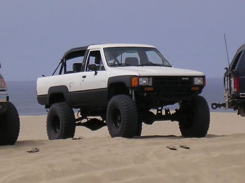 1985 Toyota 4Runner - A modified Toyota pickup truck sits on a sandy beach with the ocean in the background.