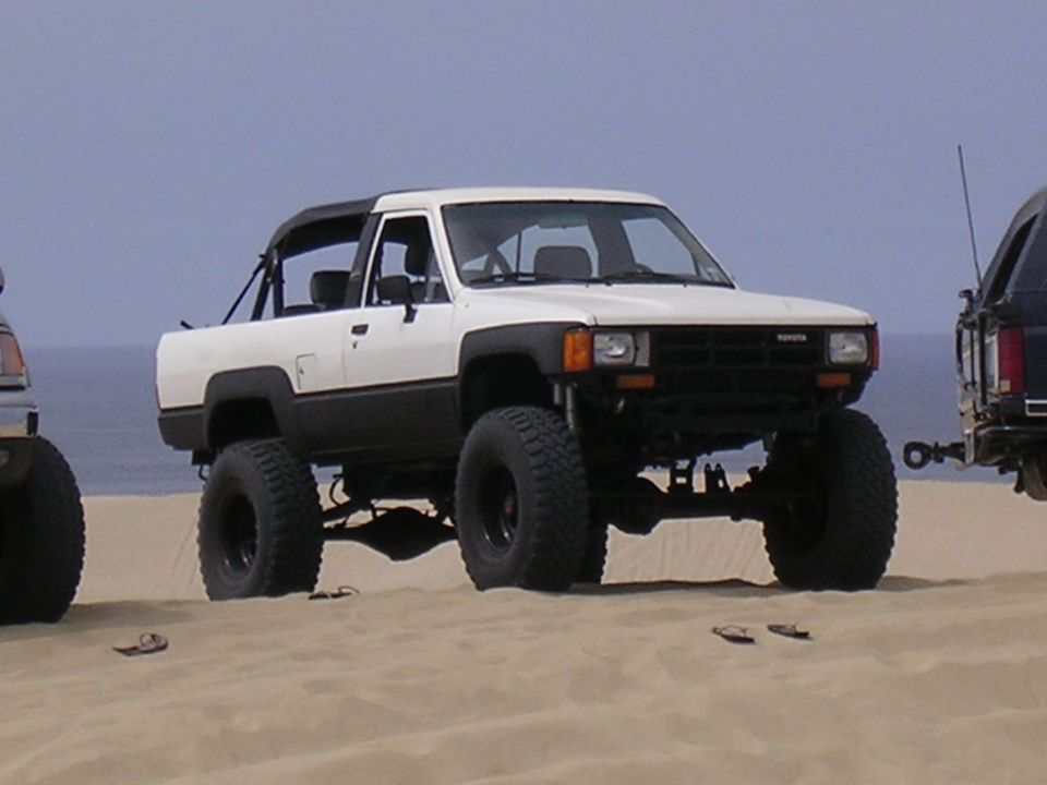 Lifted white Toyota pickup truck with black trim and soft top on sand dunes