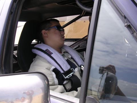 1985 Toyota 4Runner - Man in racing harness inside a vehicle with roll cage; camera reflected in window.