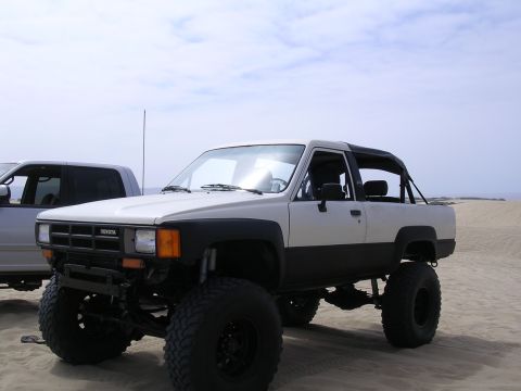 1985 Toyota 4Runner - A lifted 1985 Toyota 4Runner with oversized tires sits on a sandy beach under a cloudy sky.