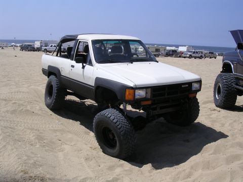 1985 Toyota 4Runner - This lifted 1985 Toyota 4Runner is parked on a sandy beach with other vehicles and RVs in the background.