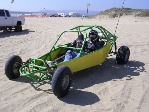 1985 Toyota 4Runner - A driver in a dune buggy enjoys a day at the beach with other vehicles and campers in the background.