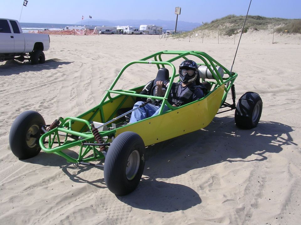 Green and yellow tube-frame sand rail dune buggy with helmeted driver on a beach