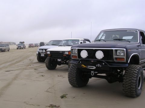 1985 Toyota 4Runner - Several modified trucks are parked on a sandy beach under an overcast sky.