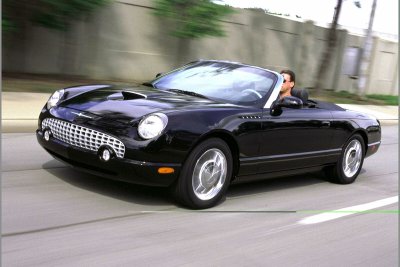 2002 Ford Thunderbird - A black 2002 Ford Thunderbird convertible is captured in motion on a paved road.