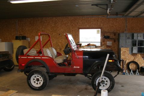 1979 Jeep CJ5 - A red and black Jeep CJ is parked inside a garage with wood-paneled walls.