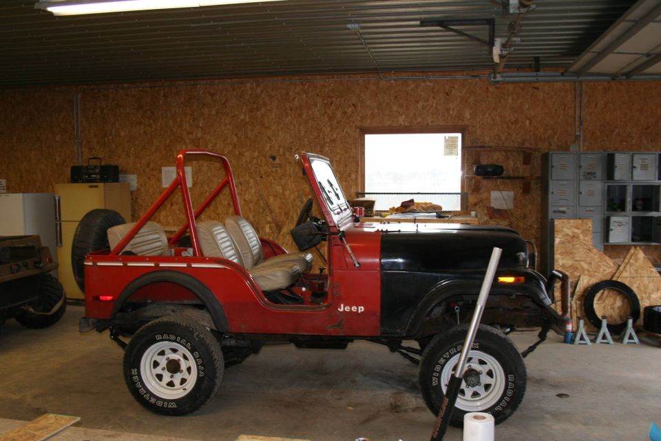 Red and black Jeep CJ in garage, roll bar, spare tire on back