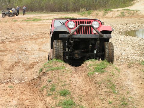 1979 Jeep CJ5 - Red Jeep CJ-series navigates an off-road course, showing its front end and suspension.