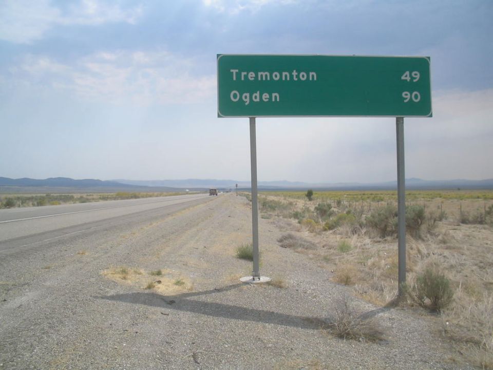 Green highway sign shows Tremonton 49 miles and Ogden 90 miles. Road stretches into the distance