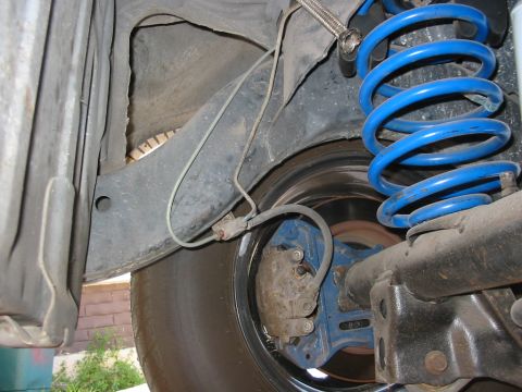 1985 Ford Crown Victoria LTD - The rear suspension and brake components of a vehicle are visible, a blue coil spring and brake caliper.