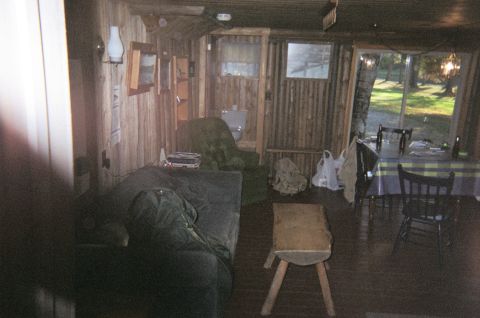 1984 Ford Bronco - A view inside a log cabin shows a sofa and chairs, with a table and chairs visible outside through a large window.