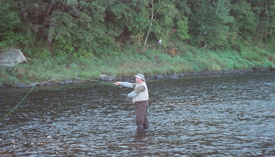 Man in waders fishing in a river with trees and rocks on the bank