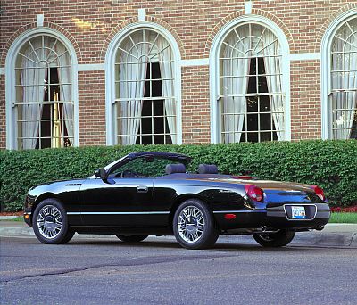 2002 Ford Thunderbird - A black 2002 Ford Thunderbird convertible is parked in front of a brick building with large arched windows.