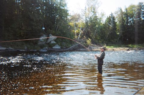 1984 Ford Bronco - Man fly fishing in a river surrounded by trees and rocks.