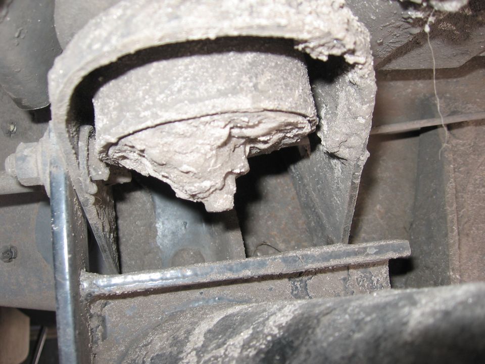Close-up of a dirty, damaged rubber suspension bushing attached to metal brackets