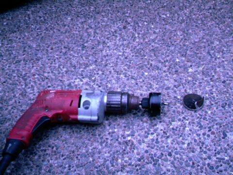 1987 Ford Bronco II - A power drill and hole saw bit are shown on a textured ground surface.